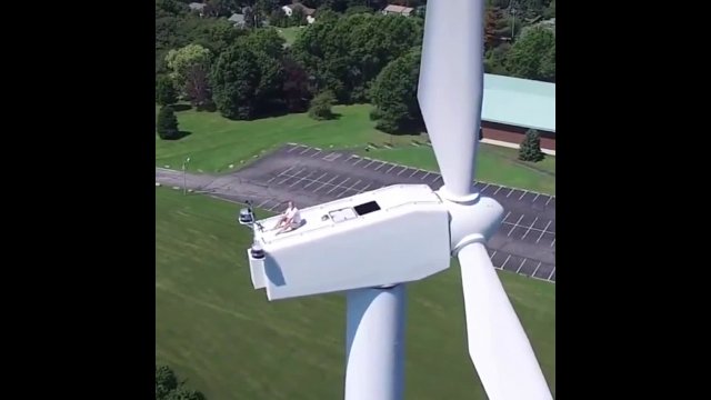 Drone captures a man sun bathing on a wind turbine with no safety on