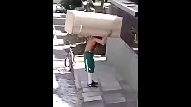 Man carry a fridge on his shoulder while riding a bike