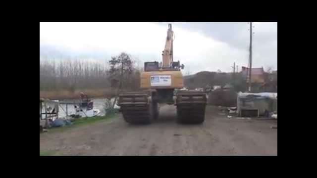 Amphibious excavator sinks, overturns, as operator clings to the tracks