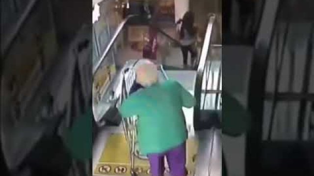 An old lady takes her wheelchair up an escalator. As she falls, she flips